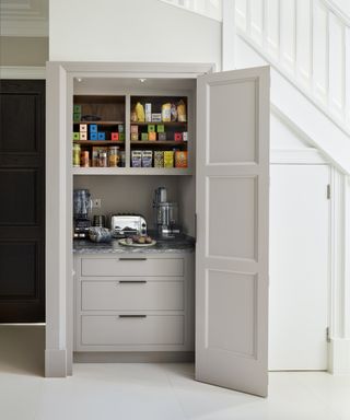 Concealed kitchen cupboard storage ideas demonstrated by a breakfast bar and shelving inside pale gray bi-fold doors.