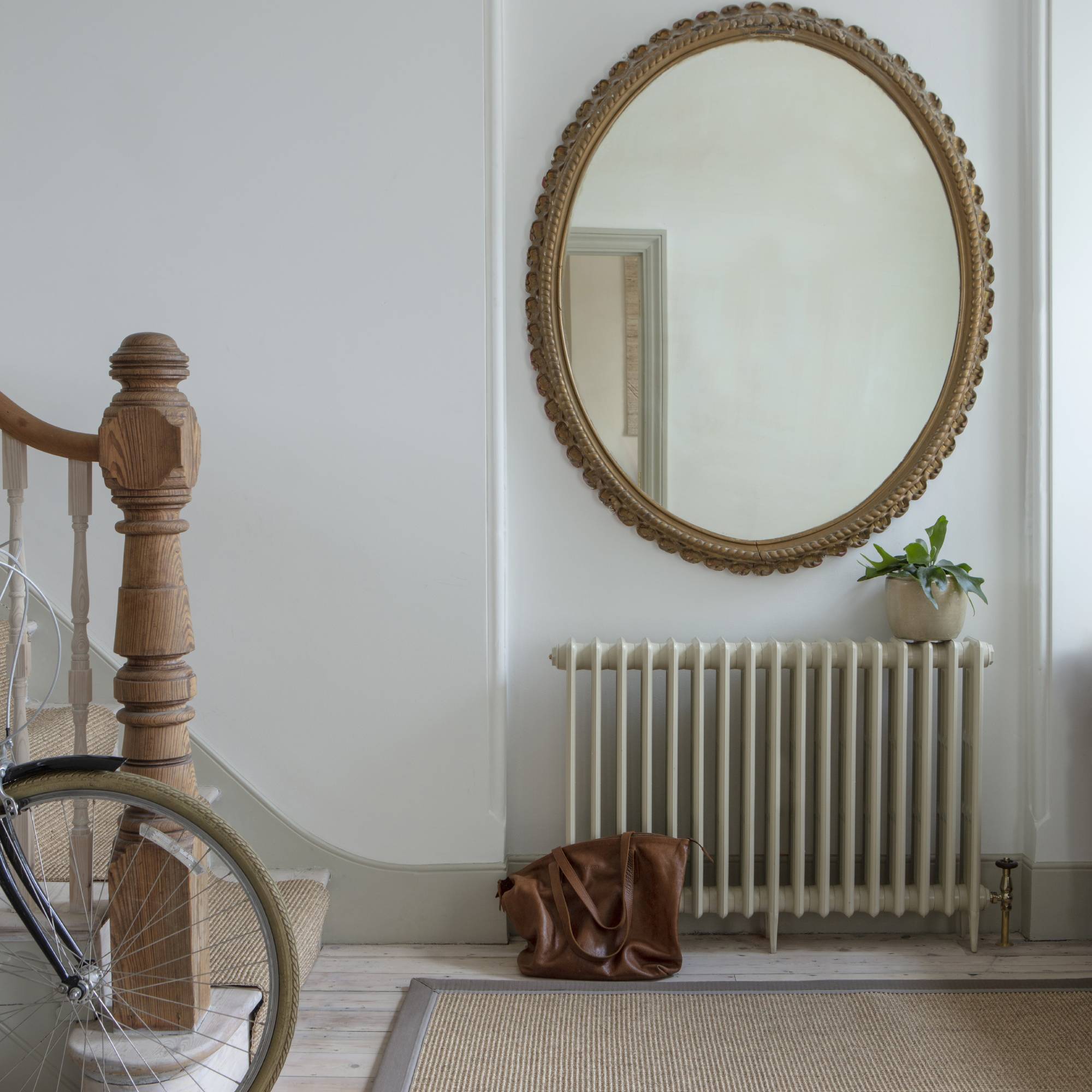 large oval mirror on hallway wall above victorian radiator and beside staircase