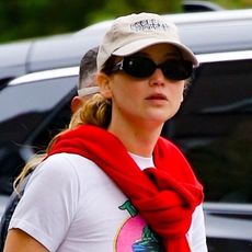 Jennifer Lawrence wearing a white tee, black pants, silver puffer shoes, and a red sweater wrapped around as a scarf while out with her family in New York City April 2024