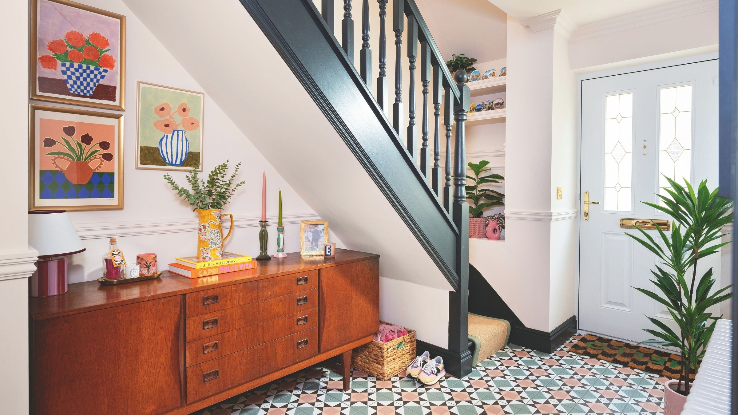 Large hallway with mid-century cabinet, colourful prints, tiled floor and painted bannister