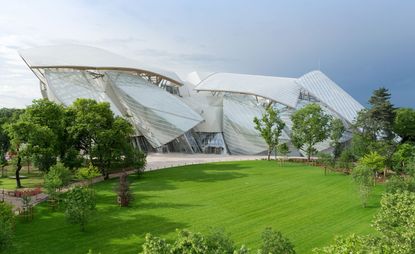 The new Louis Vuitton Foundation in Paris opens its doors to the public today. A large white building made of sail like structures with green grass and trees all around it.