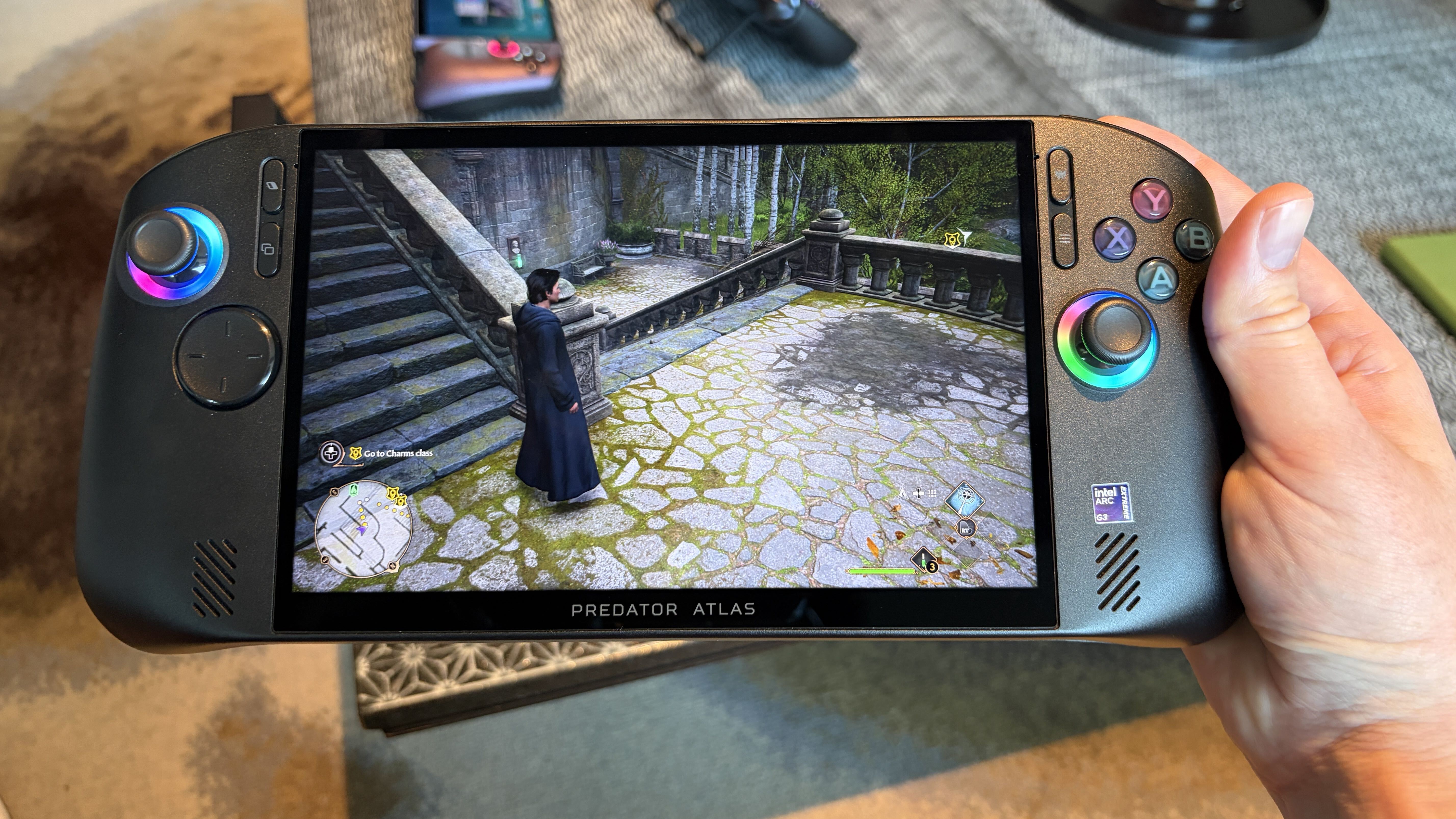 A person holding a handheld gaming device displaying a video game character on screen, with the label "PREDATOR ATLAS" below.