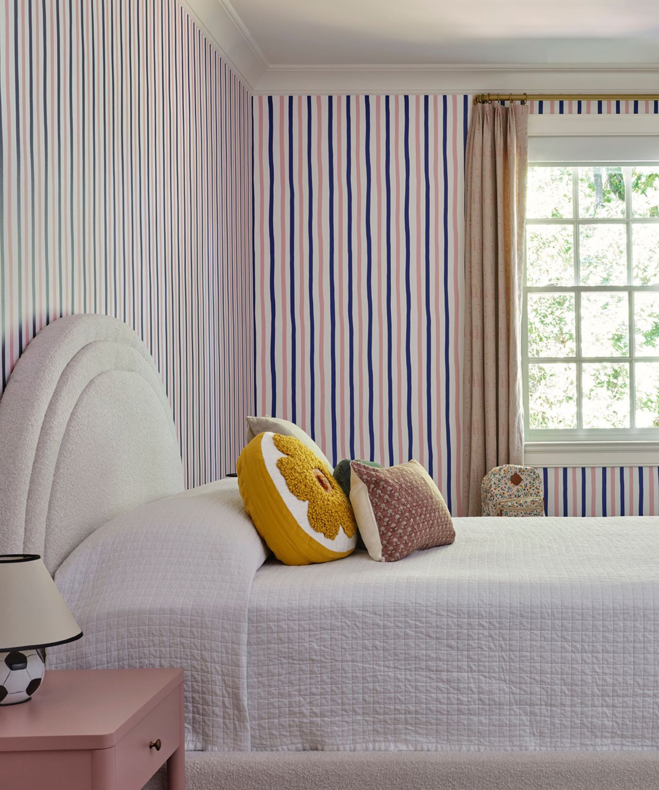 A bedroom with striped wallpaper and a boucle headboard