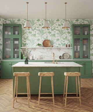 Mid-green and marble effect countertop, glazed wall units, green crane wallpaper, trio of pendant lights, bar stools, and light herringbone wood floor