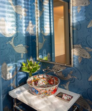 Bathroom with fish wallpaper in blue, silver mirror, decorative basin on white countertop,