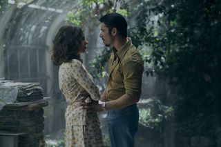 a woman (Sofia Vergara as Griselda) stands with her arms crossed facing a man (Alberto Guerra as Dario) placing his hand on her waist, as they stand in a glass-walled greenhouse