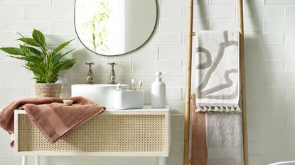 Mindful bathroom scheme with woven cane style washstand, organic shape mirror, and sculptural tasselled towels on towel ladder