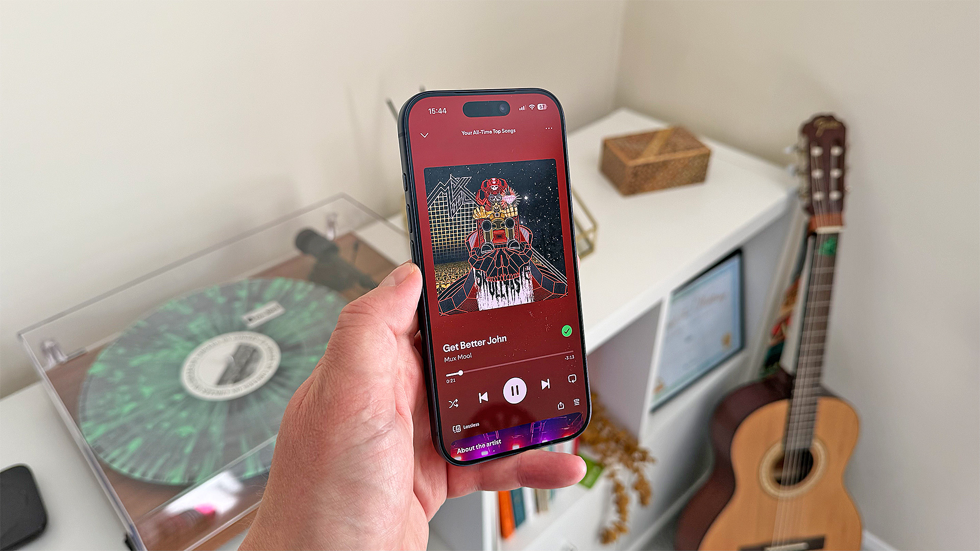Apple iPhone 17 Pro smartphone held in hand above turntable and acoustic guitar