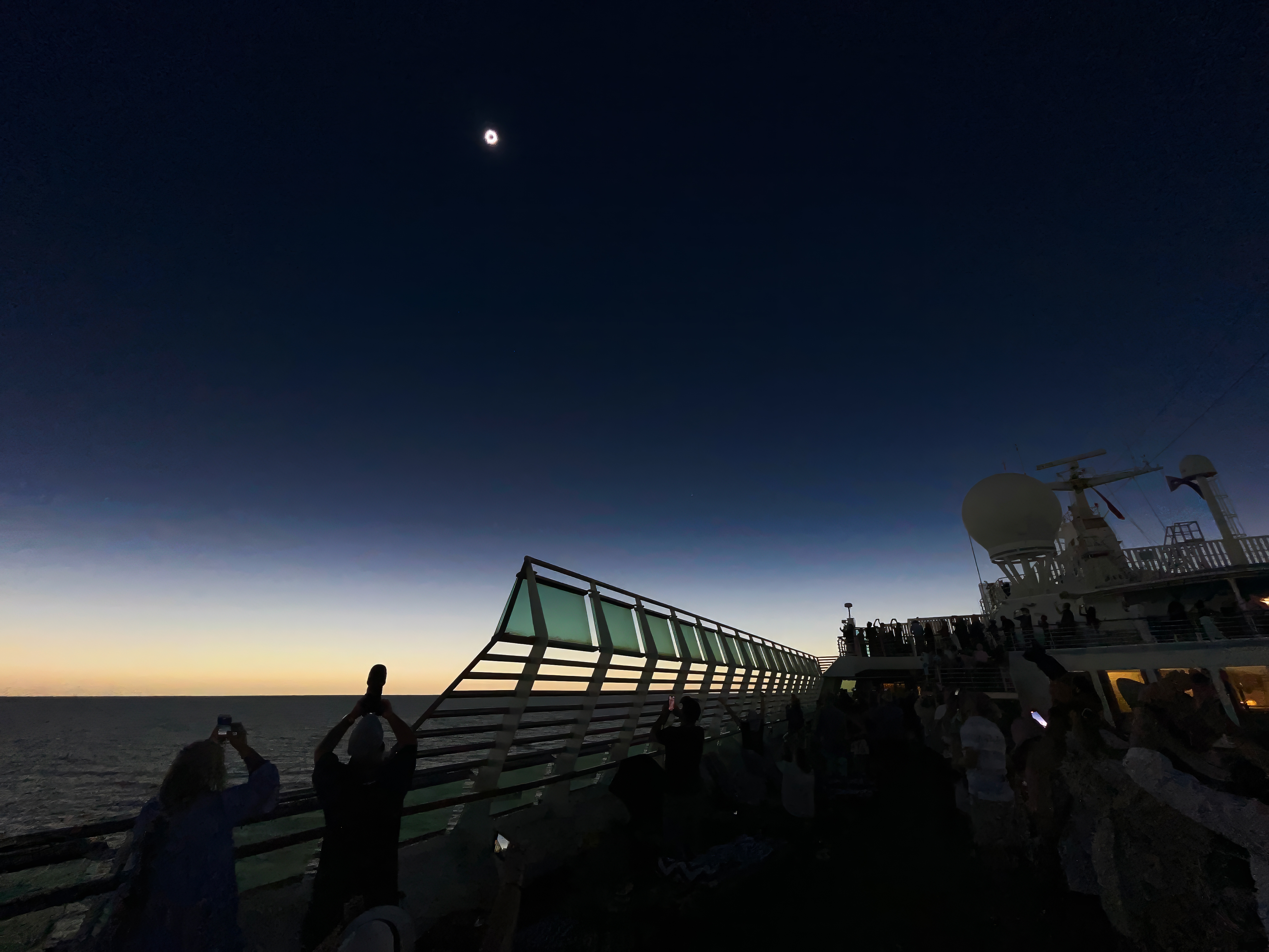 People photographing solar eclipse with their mobile phones from a ship