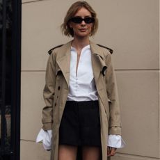 paris fashion week spring 2025 attendee wearing trench coat black skirt sunglasses and white button down shirt 