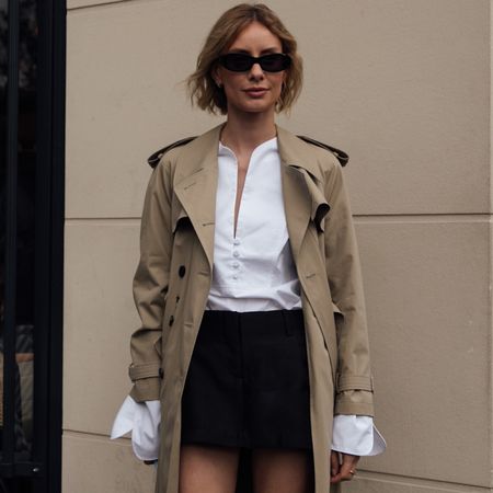 paris fashion week spring 2025 attendee wearing trench coat black skirt sunglasses and white button down shirt 