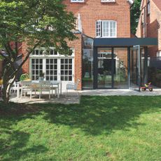 Grass lawn in back garden next to patio seating area with white garden furniture