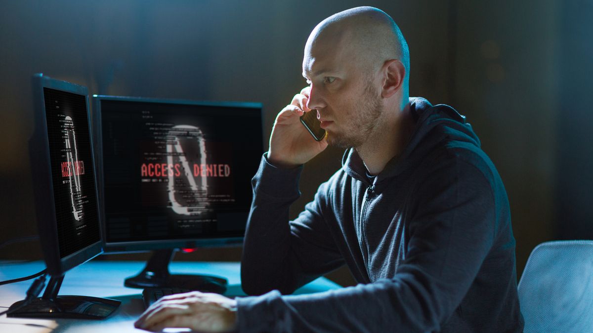 A fraudulent call centre agent in a dark room surrounded by monitors