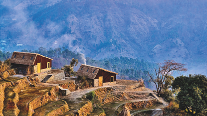 A couple cottages nestled on a Himalayan peak with other mountains in the background