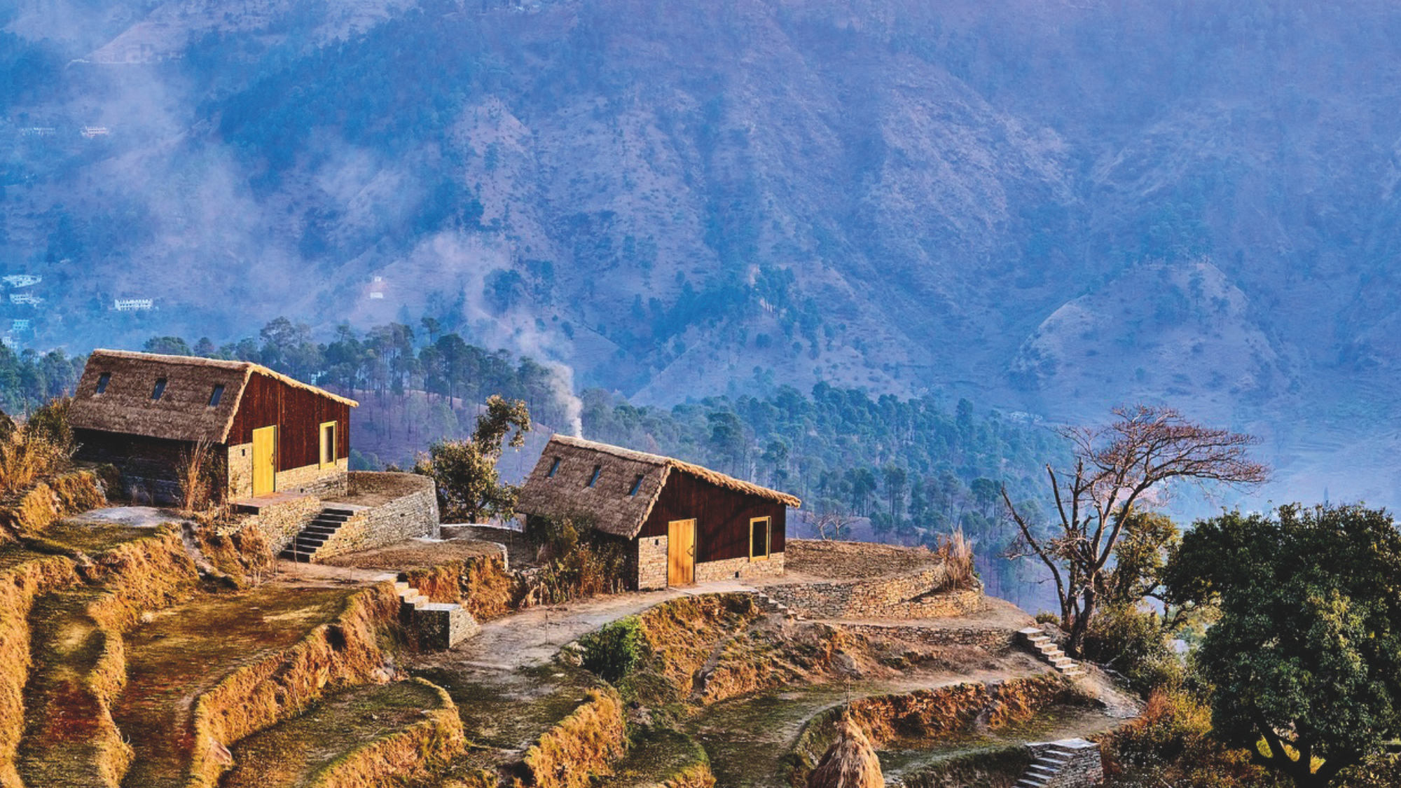 A couple cottages nestled on a Himalayan peak with other mountains in the background