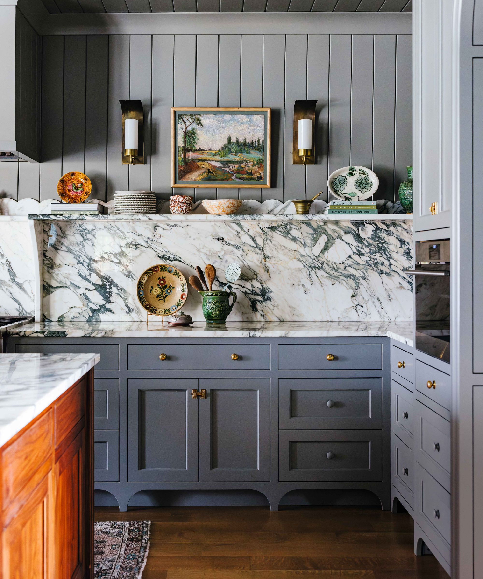a blue gray layered kitchen with bold marble counter and backsplash, open shelving with scallop detail and paneled walls