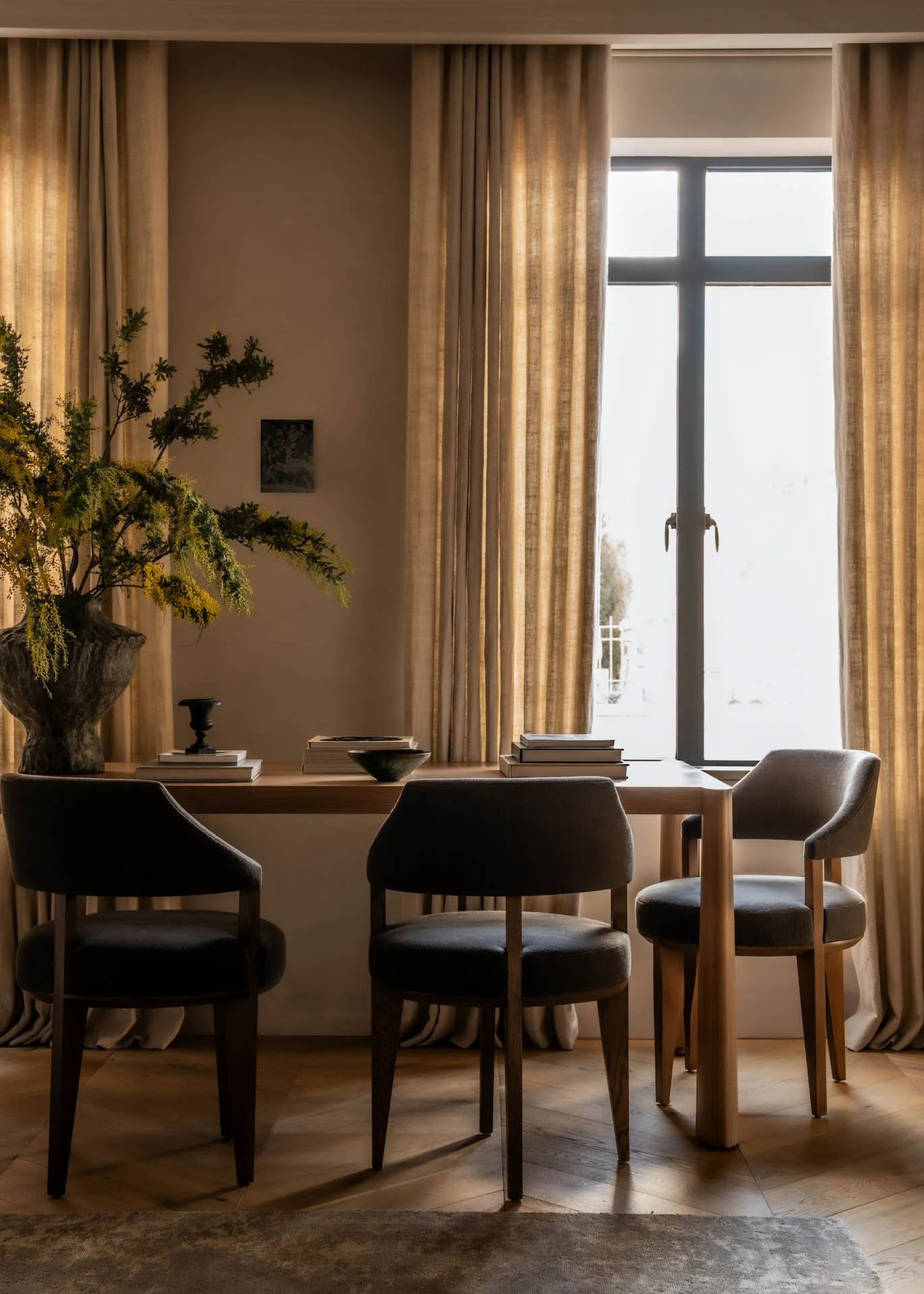 A beautiful dining room with brown beige sheer window treatments a dining set with a vase of stems and a stack of books