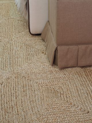 Close-up image of a jute rug. There is the corner of a skirted sofa in view.