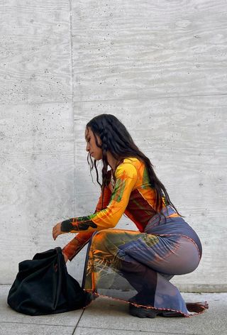 a photo showing what to wear to a rap concert with a woman wearing a gold chains over a sheer maxi dress with chunky black sneakers and a black hobo bag