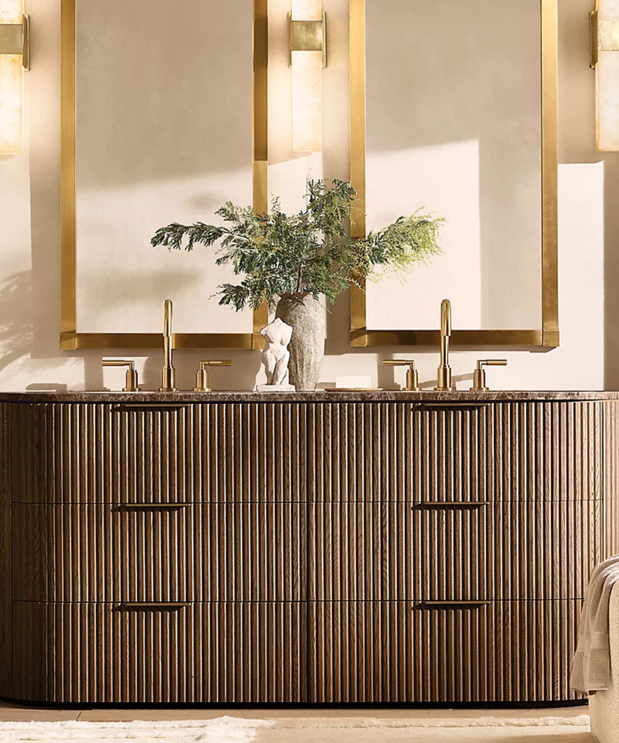A neutral bathroom with a dark fluted wood vanity and gold mirrors