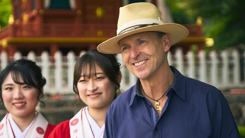 Phil waits on the mat for the first finishers in Leg 1 of The Amazing Race Season 37 in a straw hat.