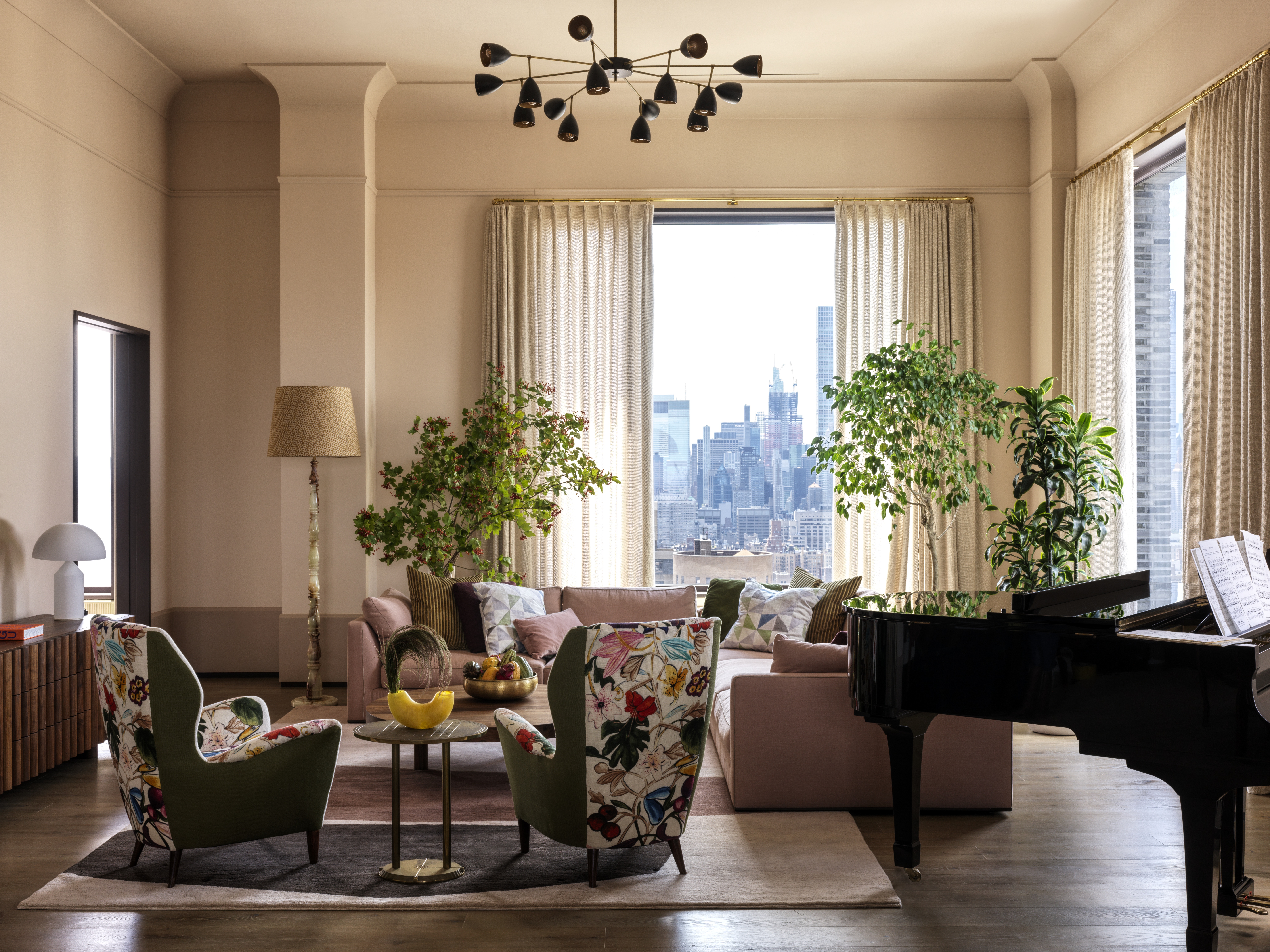modern living room with piano, pink walls, floral patterned armchairs, tall potted trees, floor lamp and pink sofa