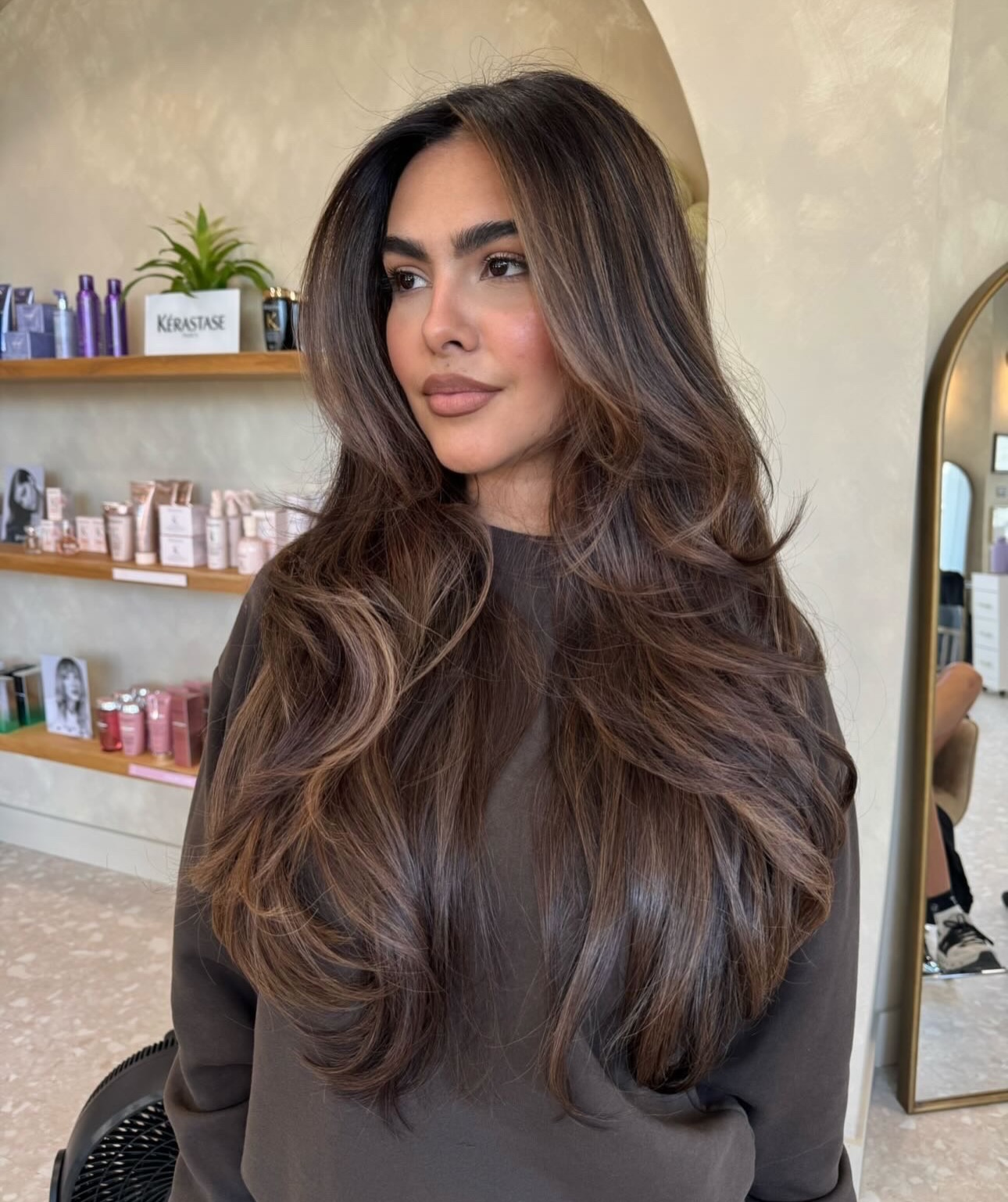 a woman in a hair salon with long, layered hair featuring espresso brunette hair color