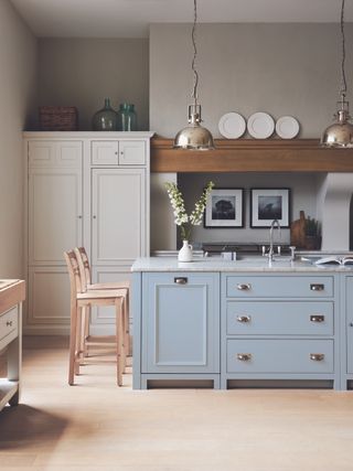 A baby blue kitchen island in a pale gray scheme with wooden bar stools, marble countertops and pale wooden flooring.