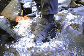 A black hiking shoe submerged in water in a riverbed