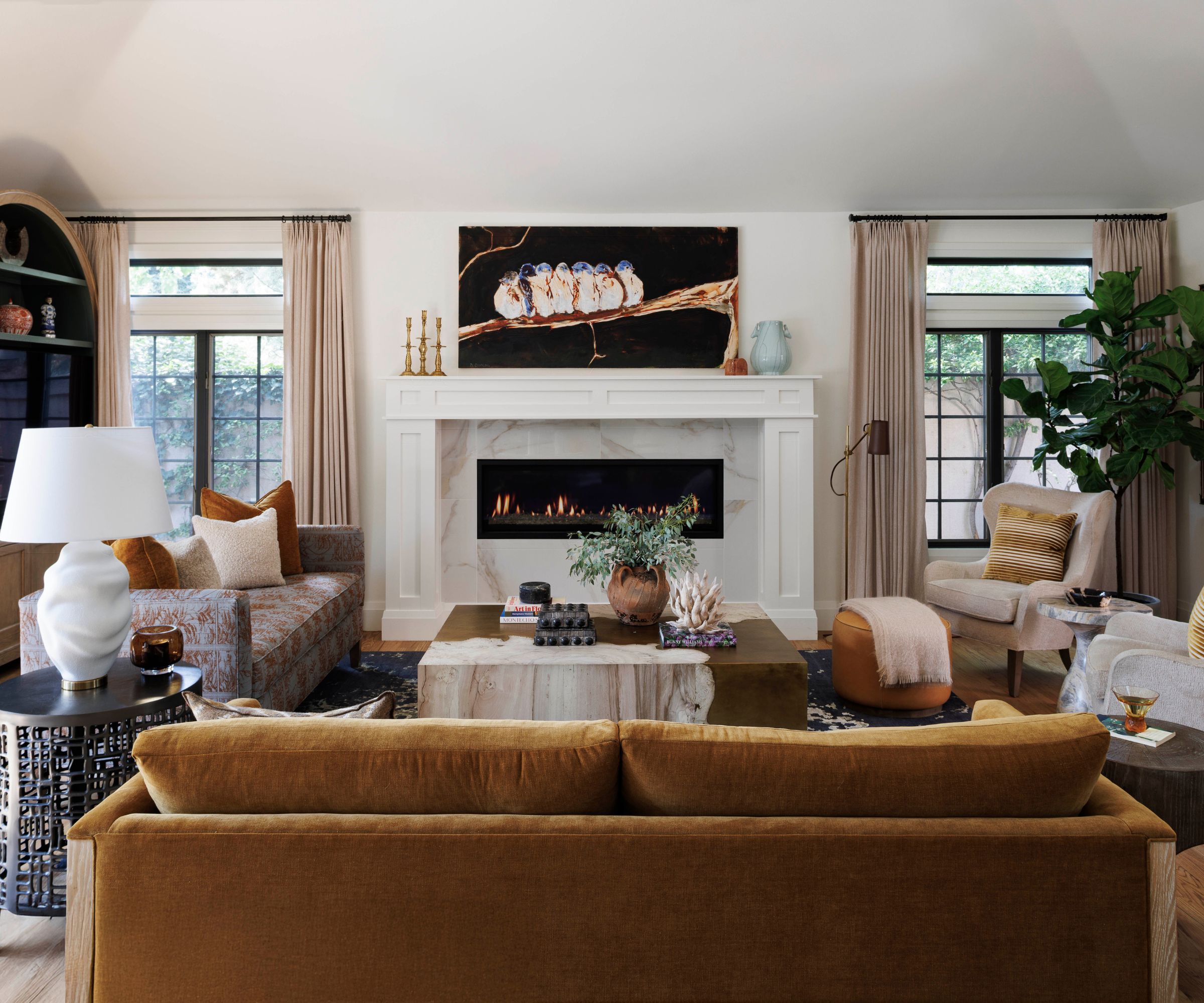 White living room with yellow velvet sofa, marble fireplace, marble coffee table, side tables with lamps and a fiddle leaf fig tree in the corner