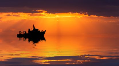 A research ship at sea at sunset.