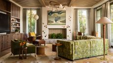 modern living room with timber panelled ceiling, patterned rug, fireplace filled with plants with wall decor and large artwork, built-in timber joinery with TV and shelves, vintage armchairs, side tables, floor lamp, and a patterned sofa 