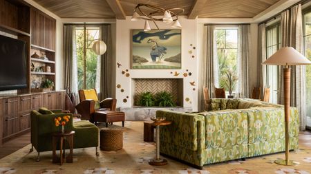 modern living room with timber panelled ceiling, patterned rug, fireplace filled with plants with wall decor and large artwork, built-in timber joinery with TV and shelves, vintage armchairs, side tables, floor lamp, and a patterned sofa