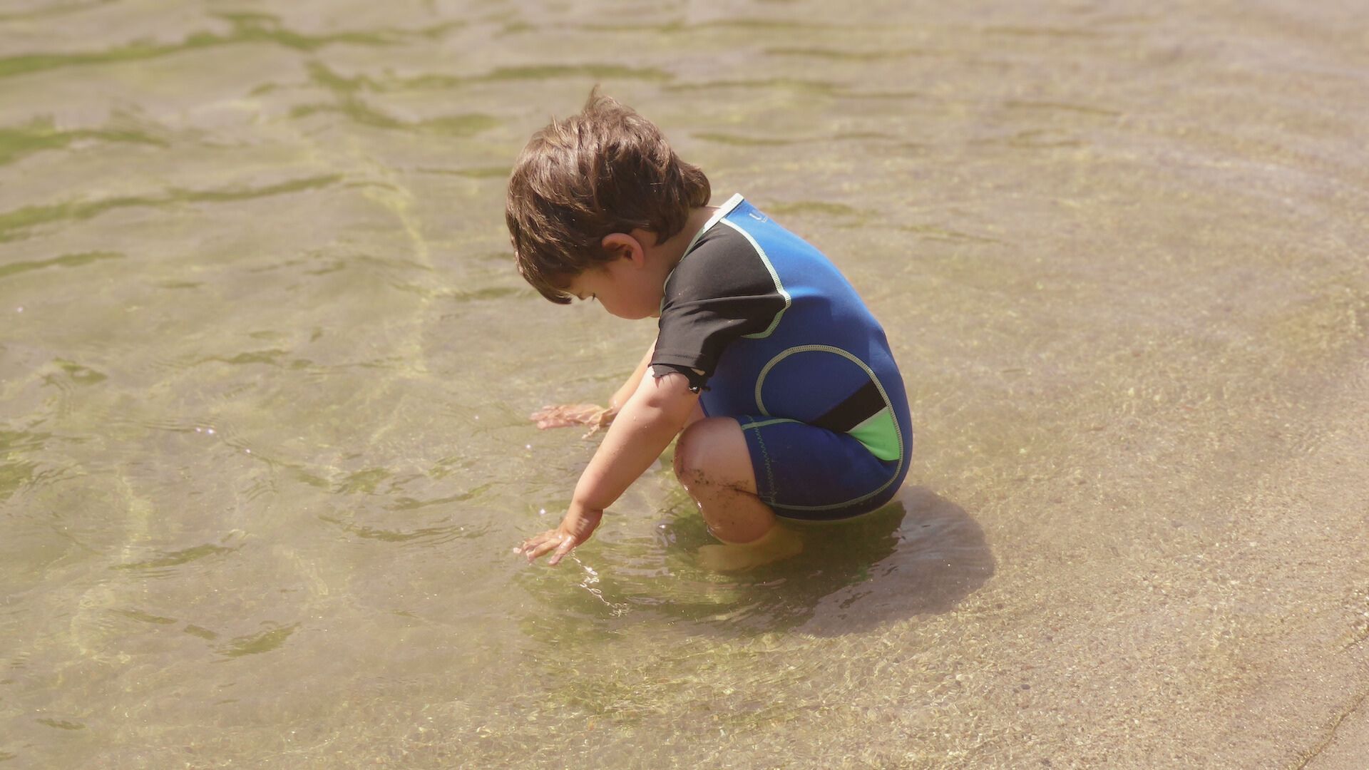 a young boy with a glucose monitor on his arm plays in the water