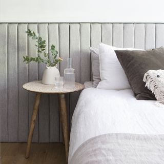 Bed next to sage green wall panelling with white bedding and a wooden bedside table.