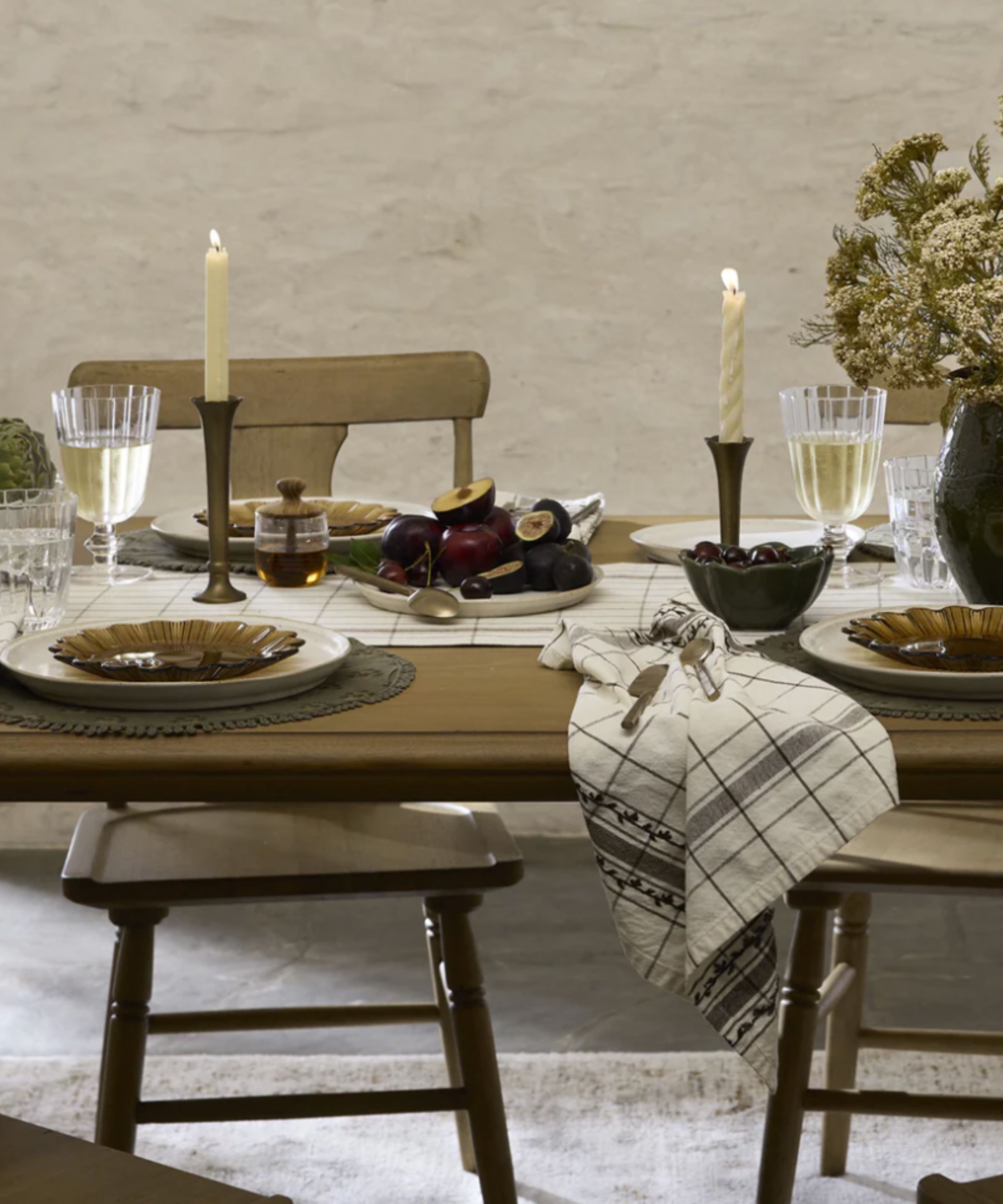Natural table setting with candles, figs in the center, dried flowers in a vase and scalloped plates