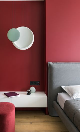A bedroom with light grey bedding and red walls
