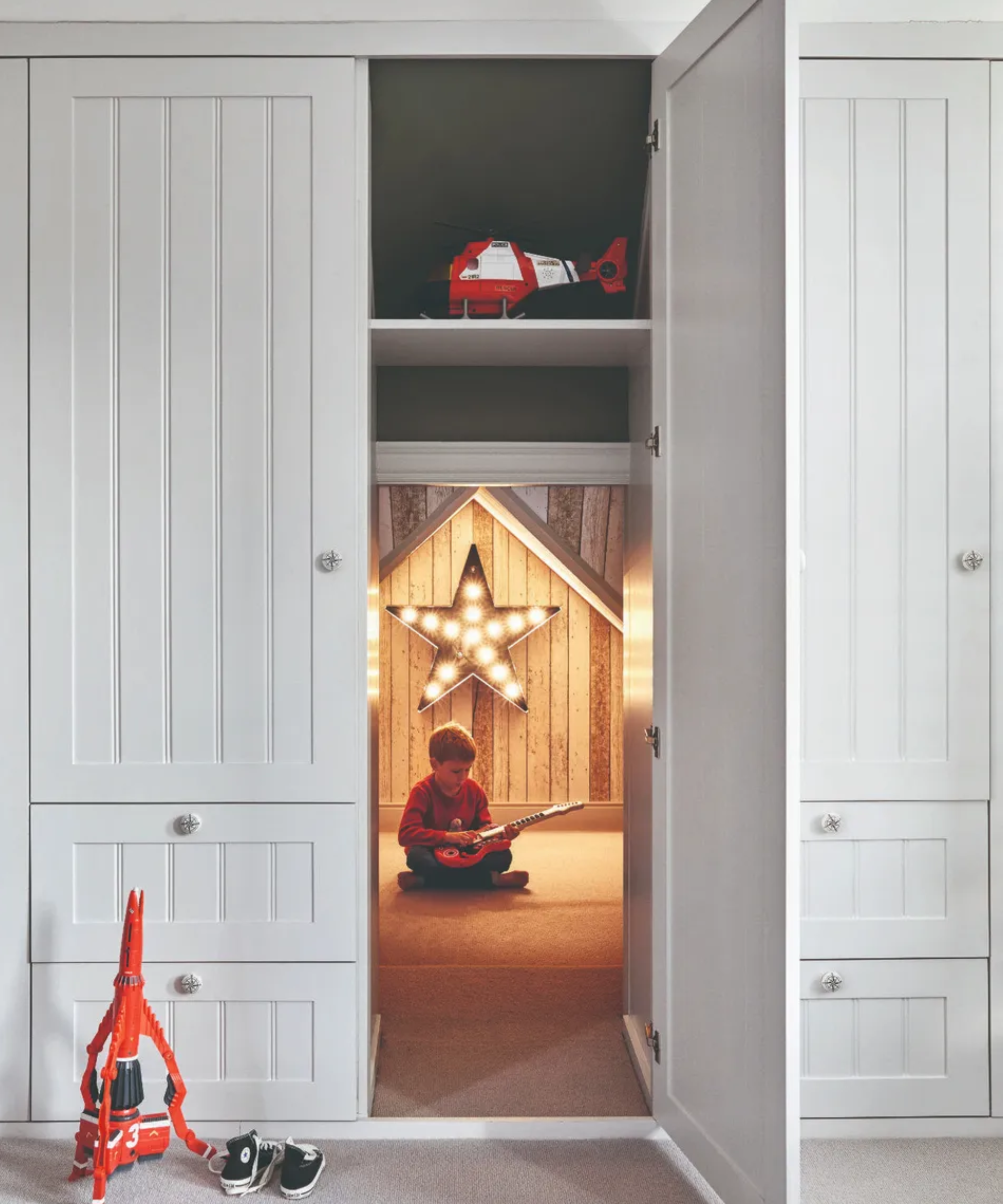 A concealed hidden room inside a wardrobe with a child sitting inside holding a guitar