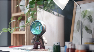 Image of a desk with mirror, plant pot and shelves in background and a centre piece of a model of a small man with fish tank for a head