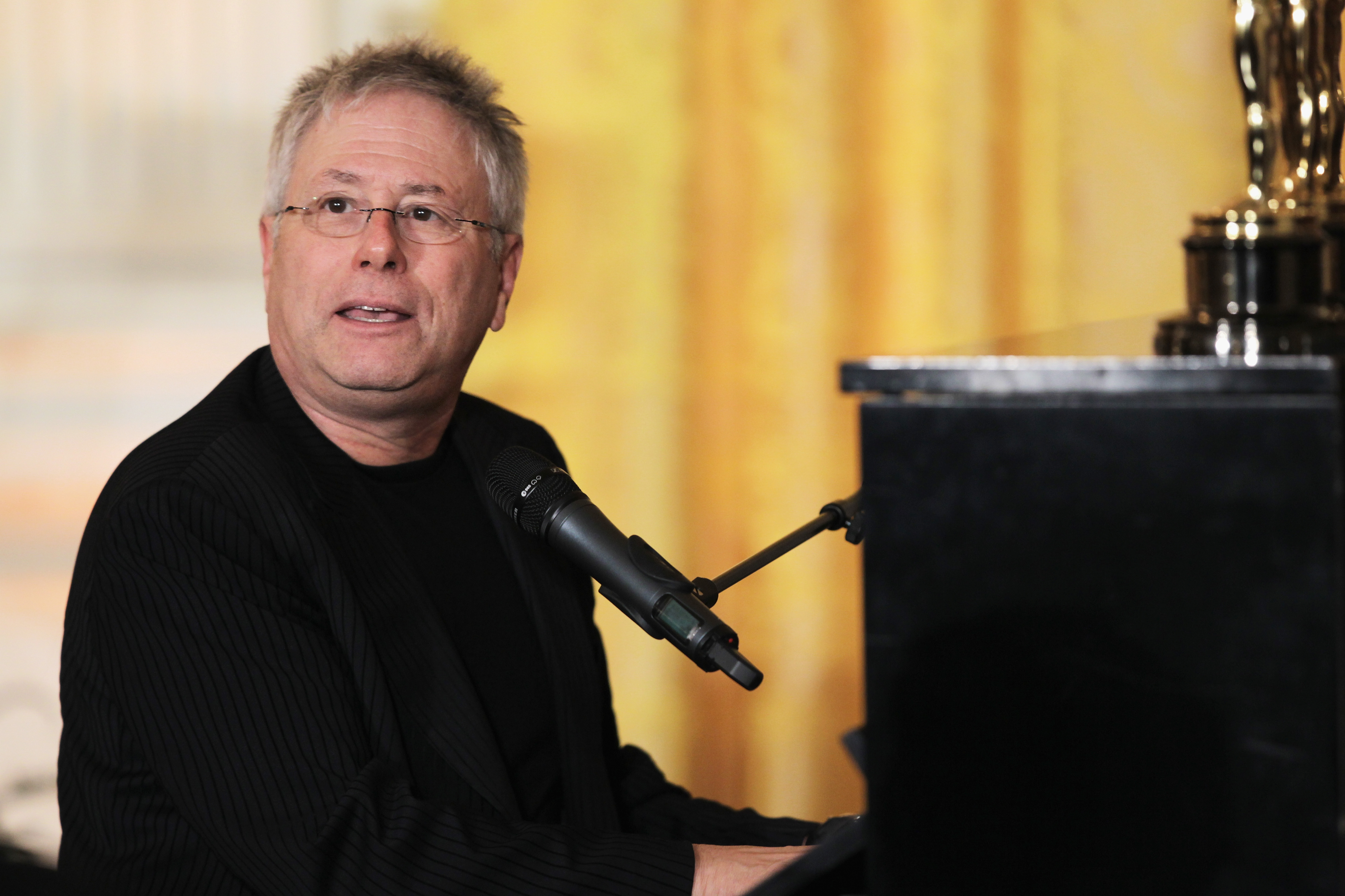 Alan Menken sitting at a piano with a microphone