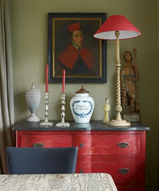 dining room, Red Flamant chest of drawers, antique French candlesticks, tobacco jar, framed portrait, tall lamp with red shade