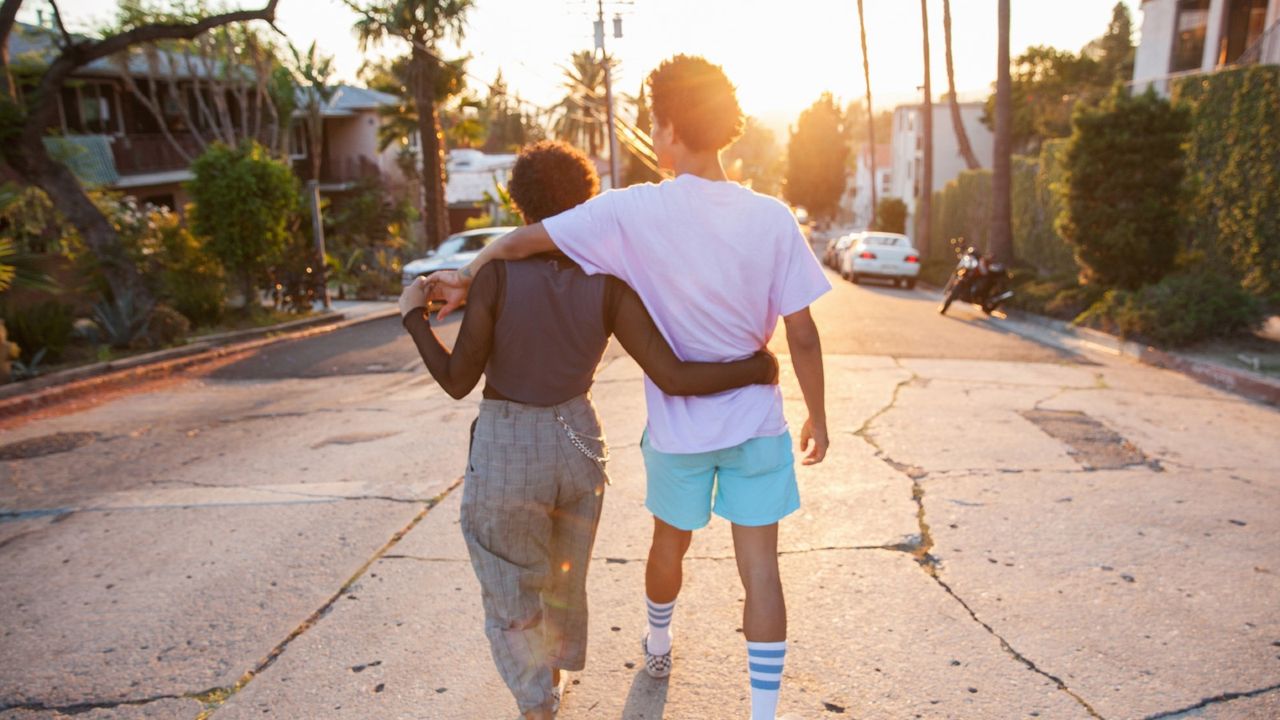 Young couple with their arms around each other walking down street - stock photo