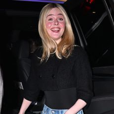 Ella fanning wears a black top with wide-leg jeans.