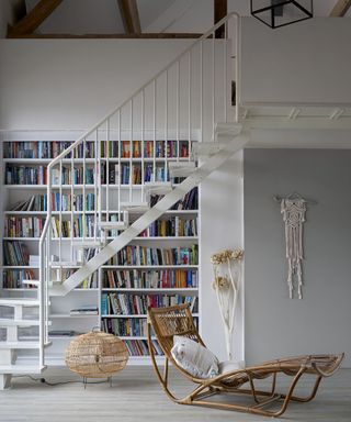 A white staircase with a home library by Carpetright with rattan chair furniture and macrame wall hanging