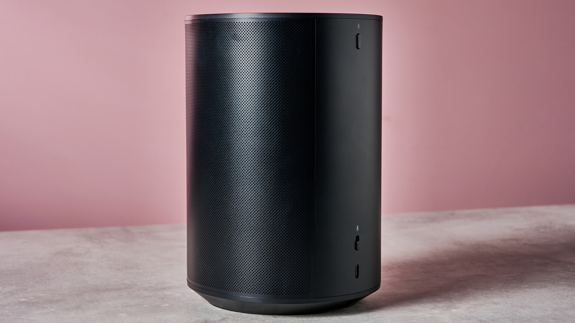 The reverse of the Sonos Era 100 showing its USB-C port and pairing button in front of a pink background.