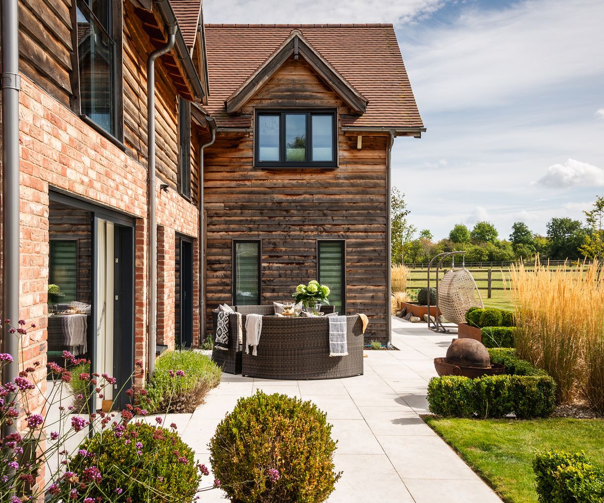 Timber and brick clad self build home with a landscaped patio and outdoor seating area