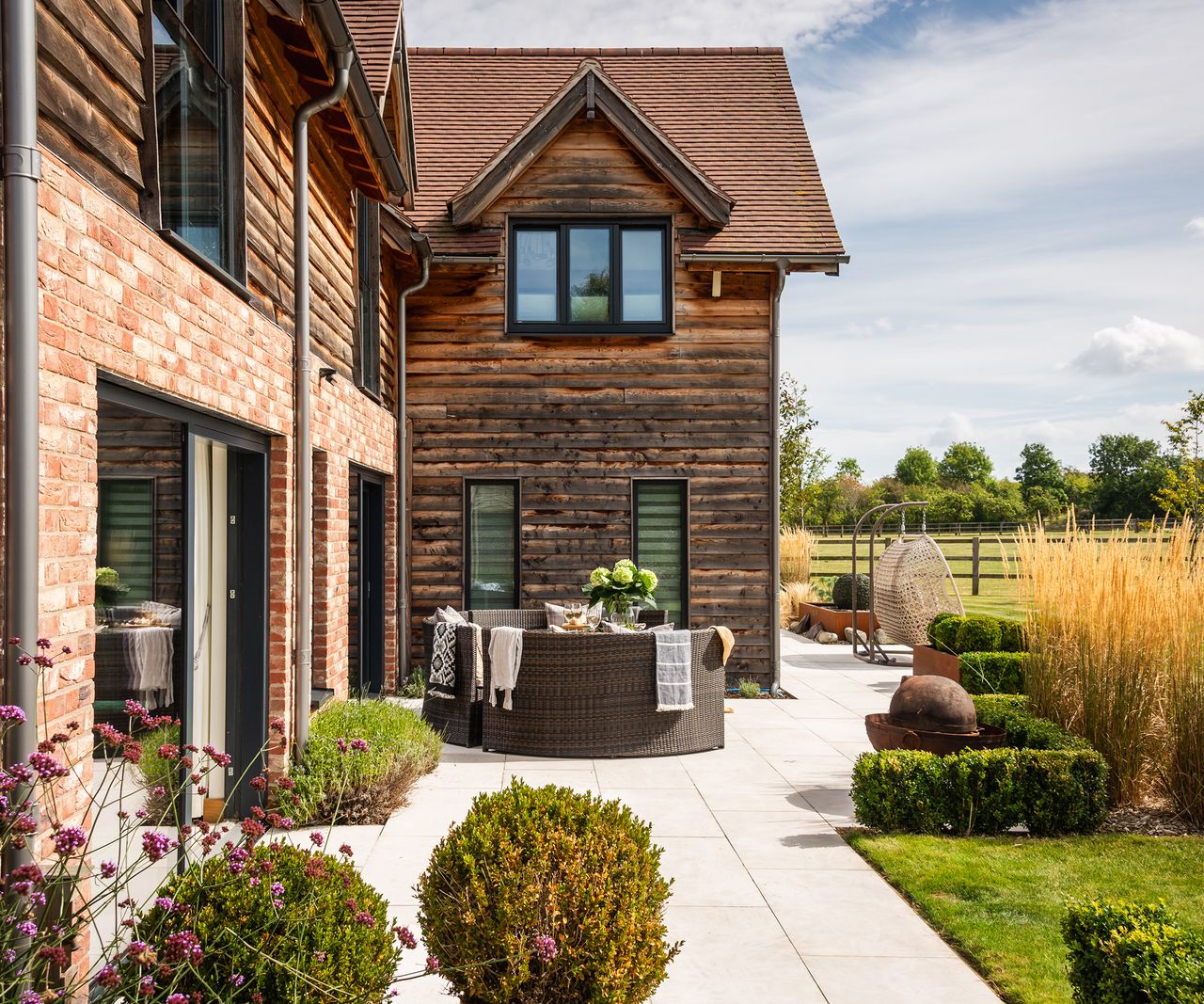 Timber and brick clad self build home with a landscaped patio and outdoor seating area