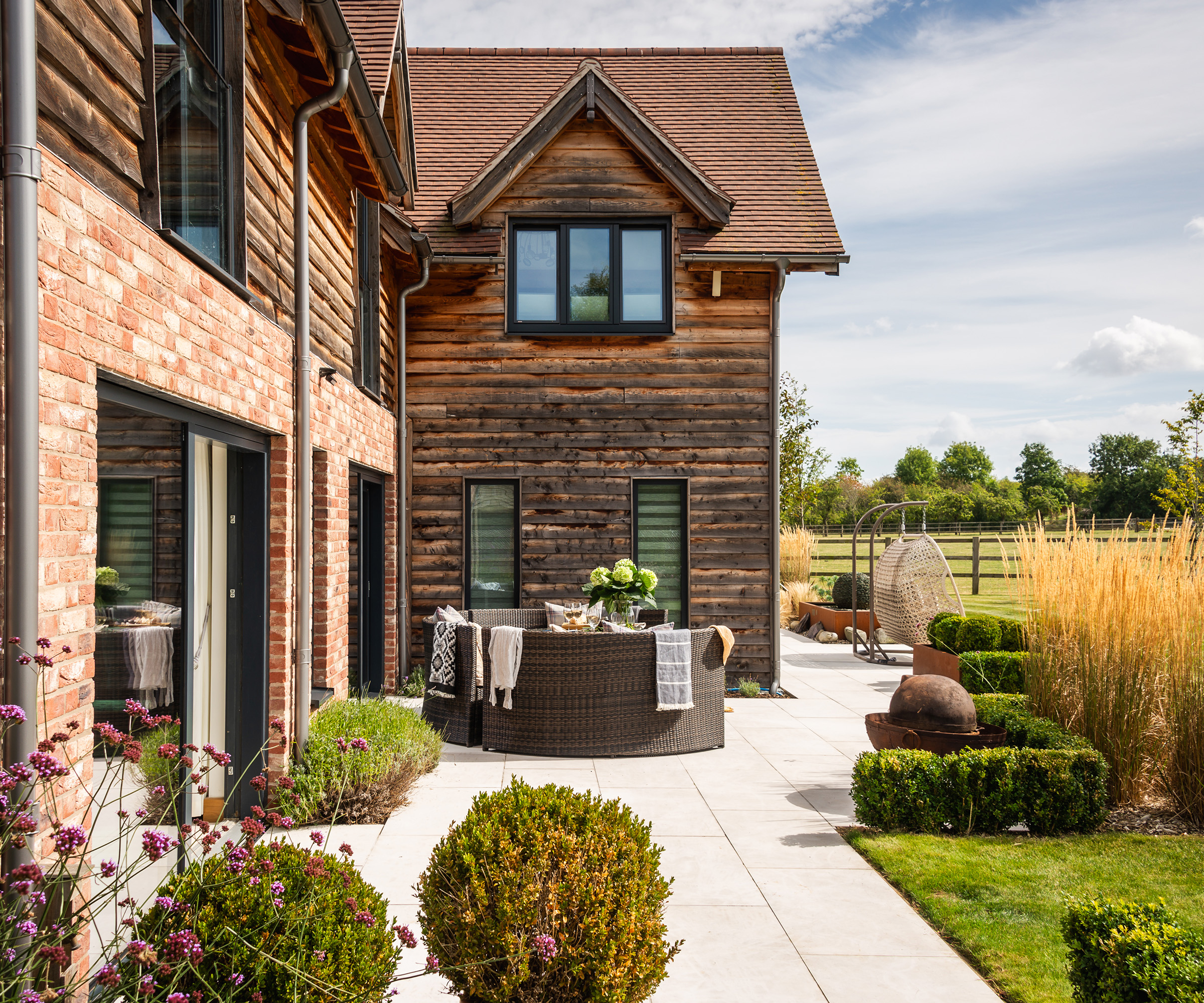 Timber and brick clad self build home with a landscaped patio and outdoor seating area