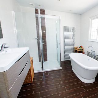 A white ensuite bathroom with brown tile-effect flooring, shower enclosure with glass door and metal heated towel rail