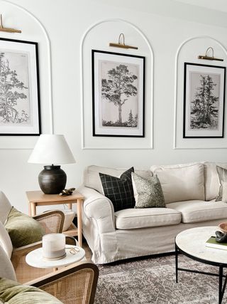 A neutrally decorated living room with molding on the walls framing pictures and brass picture lights